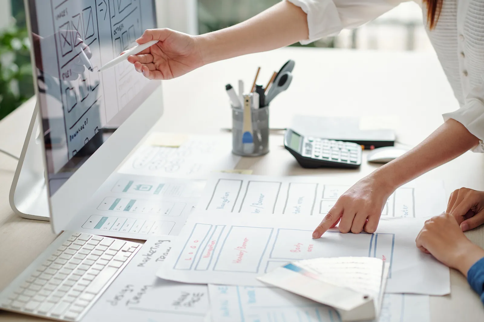 Two people pointing at printed mobile app wireframe screens spread across a desk