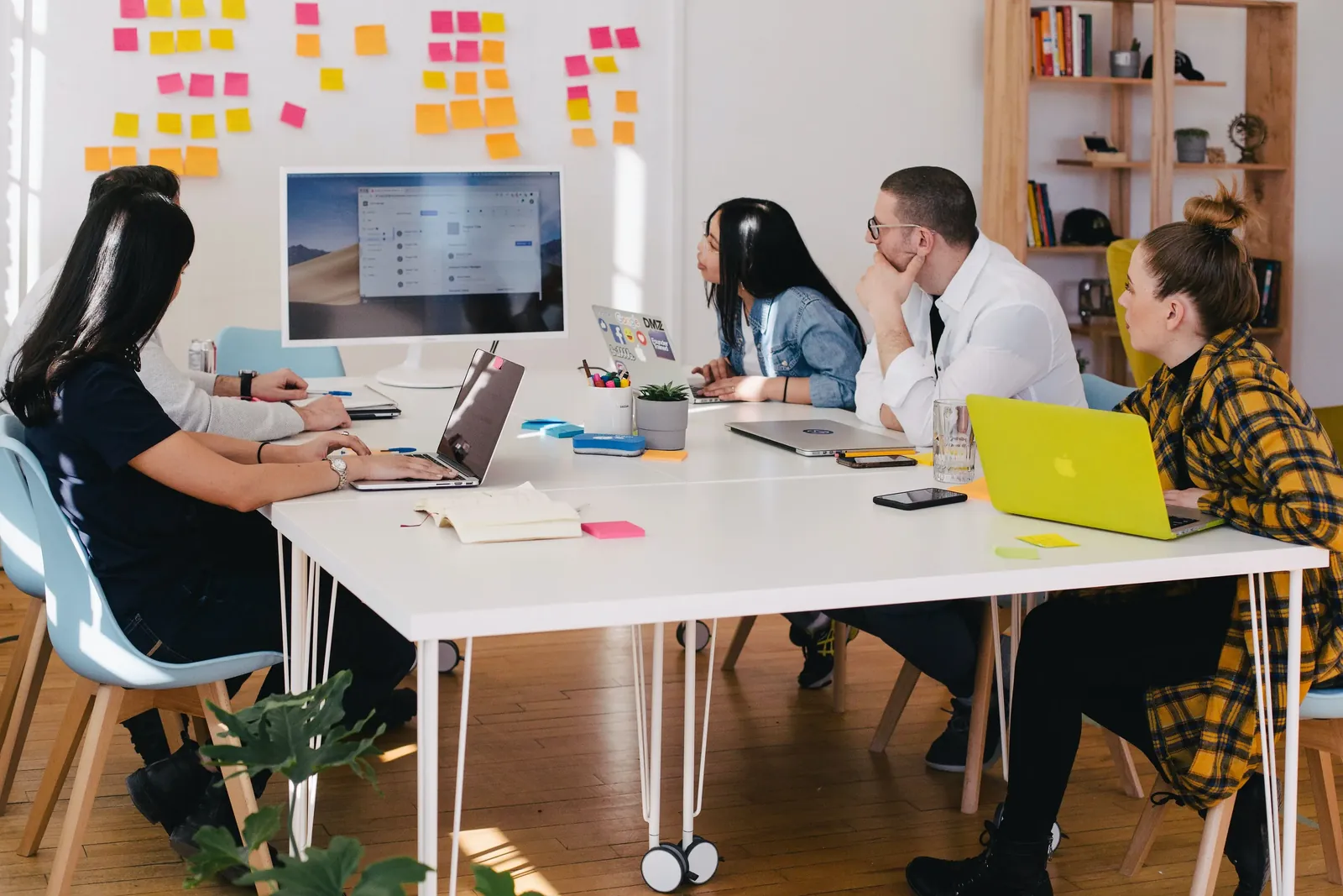 Team working at a long table of laptops beside a wall of sticky notes